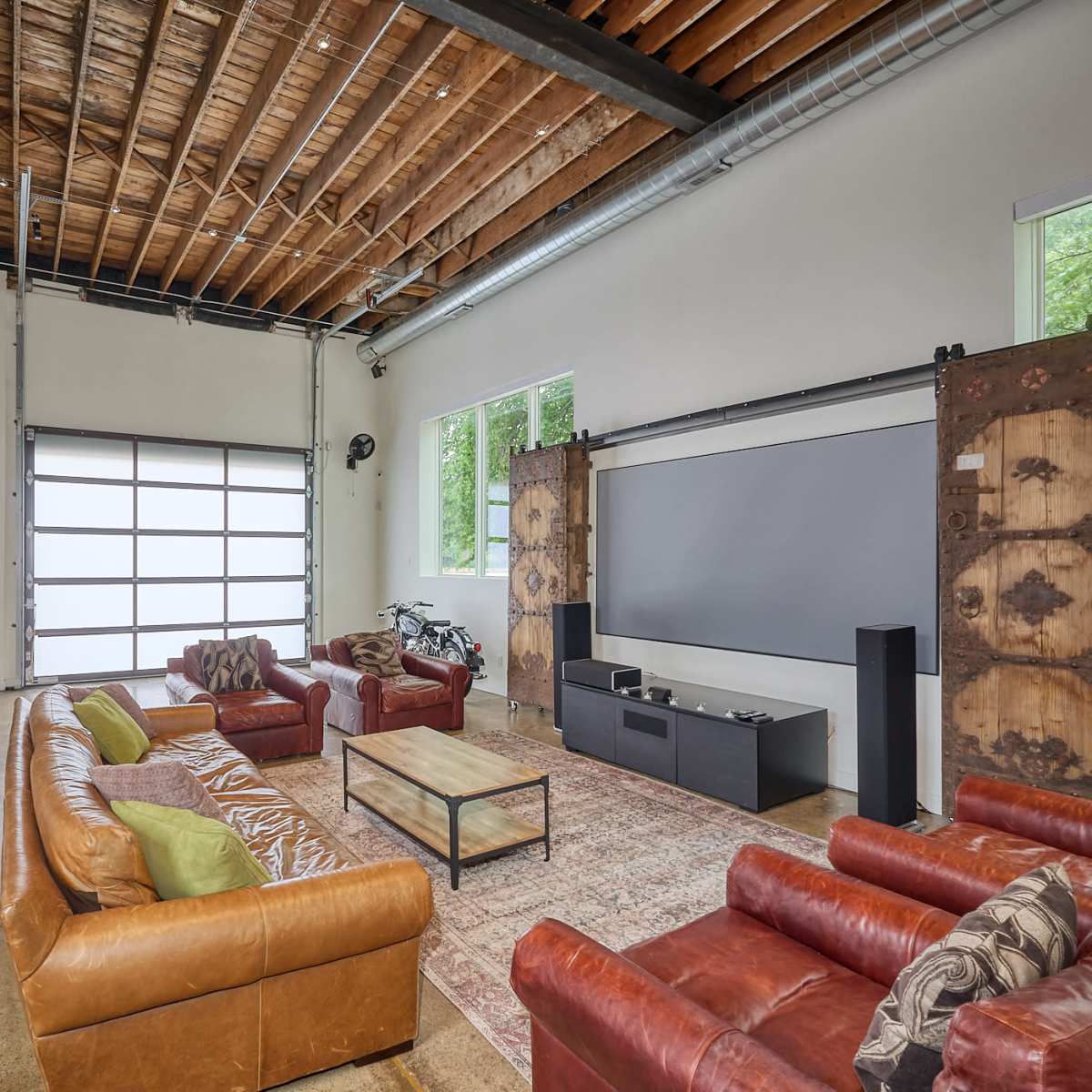 A spacious living area with leather sofas, a coffee table, a large screen on one wall, and a garage door that opens to the outside.