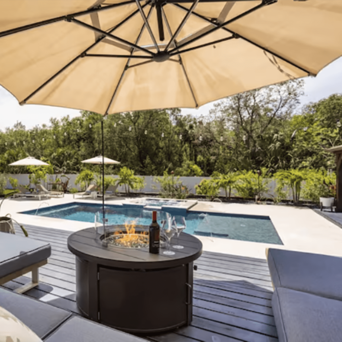 A patio area features a fire pit surrounded by lounge chairs and a swimming pool, with an umbrella providing shade.