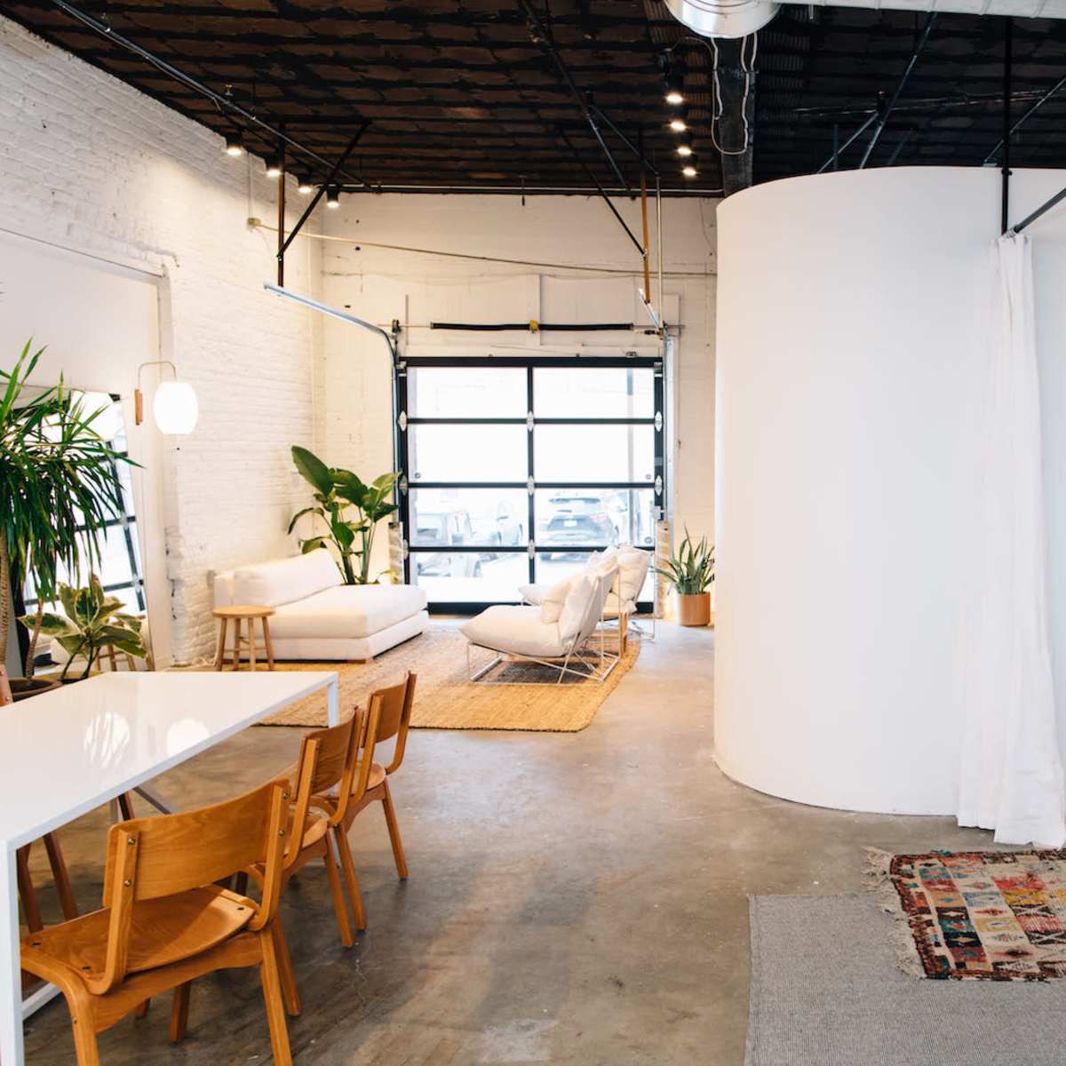 A spacious interior with a dining area featuring wooden chairs, a round partition, and various plants alongside a cozy seating area illuminated by soft lighting.