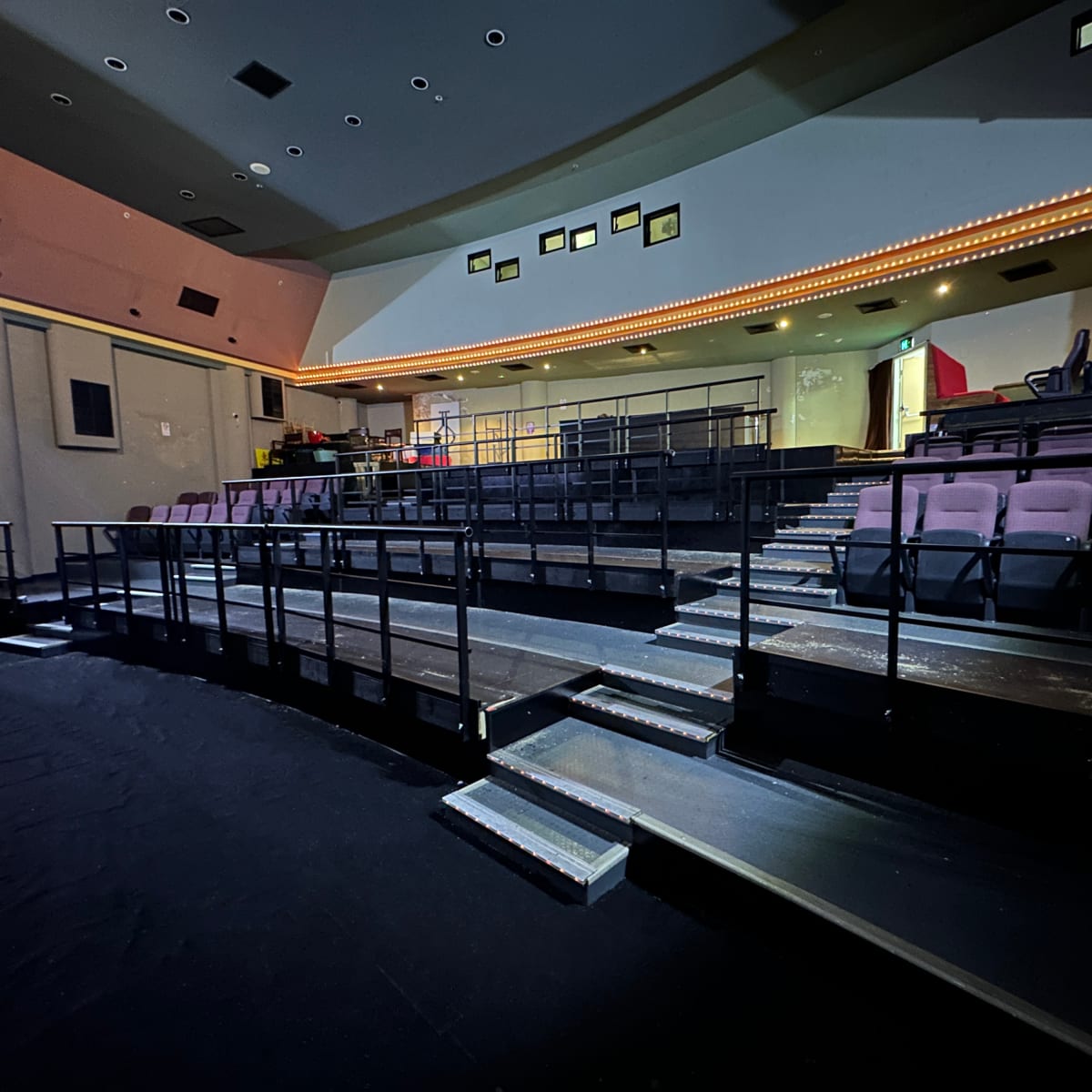 A theater interior with tiered seating, a stage area, and illuminated borders along the ceiling.