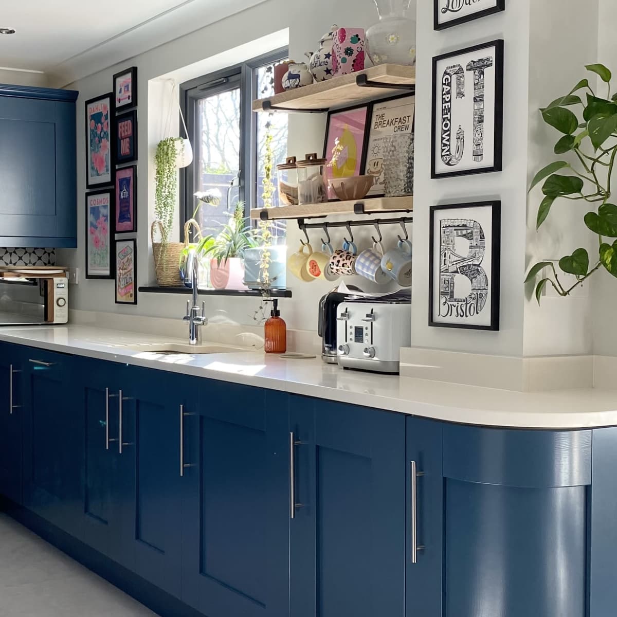 A modern kitchen with blue cabinetry, open shelves displaying decorative items, and a bright window providing natural light.