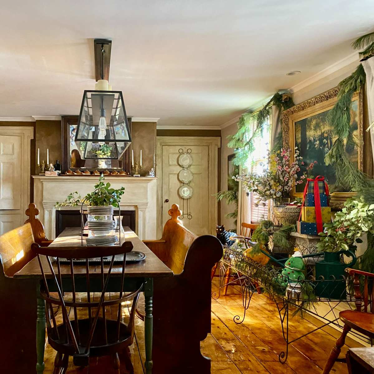 A dining area features a wooden table surrounded by chairs, with a fireplace in the background adorned with holiday decorations and greenery.