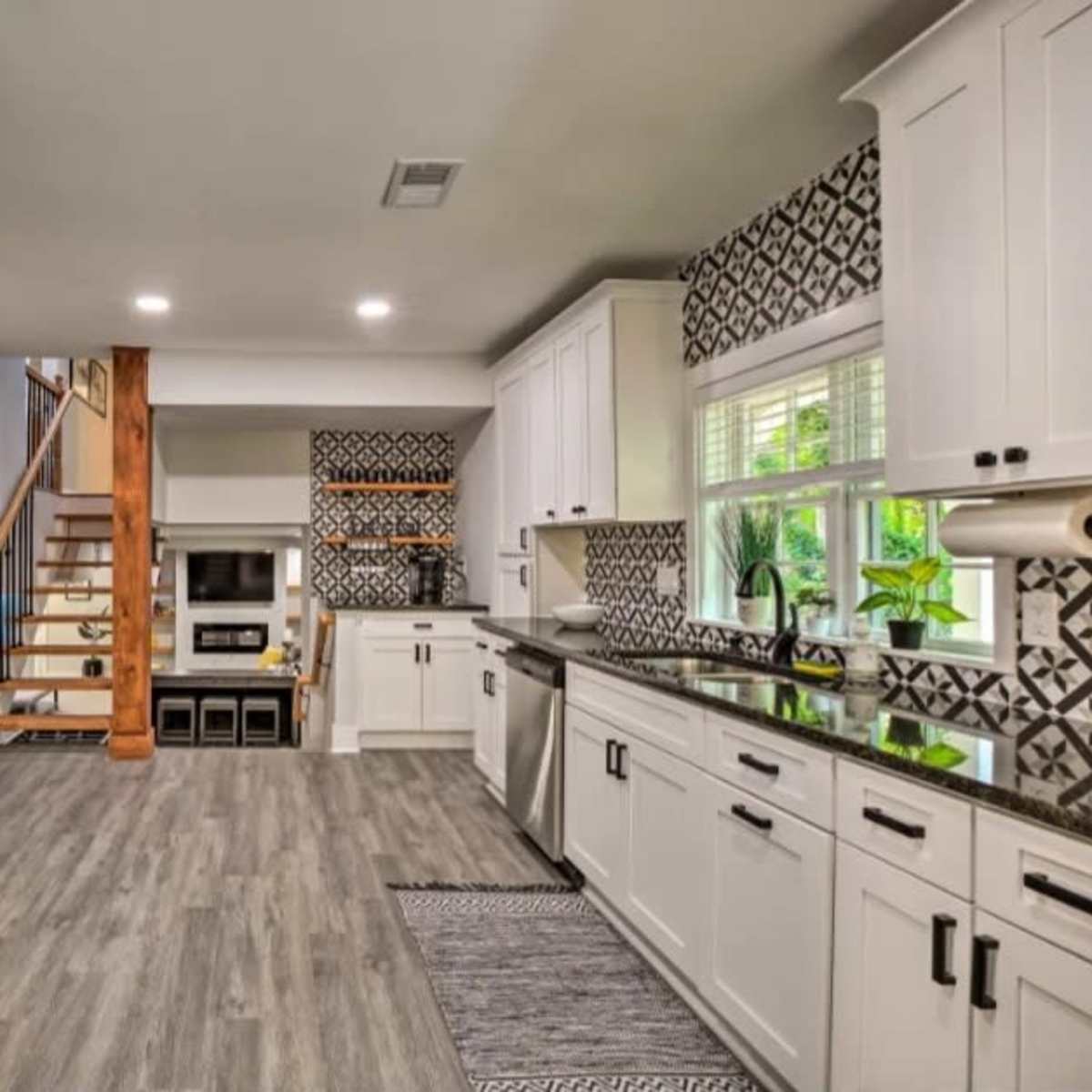 A modern kitchen with white cabinets, stainless steel appliances, and a patterned backsplash, featuring an open layout that connects to a staircase and living area.