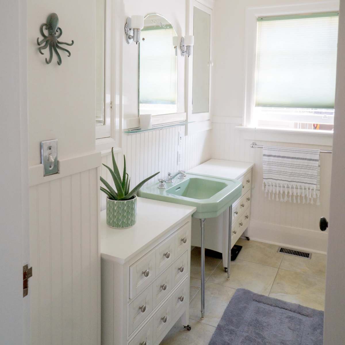 A bright bathroom features a mint green sink, white cabinetry, a wall-mounted mirror, and an octopus decoration.