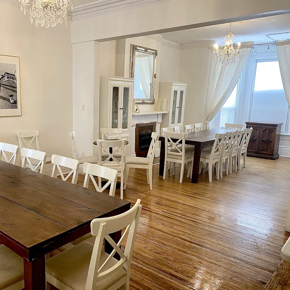 A spacious dining area with large wooden tables, white chairs, and light-colored walls, illuminated by natural light.