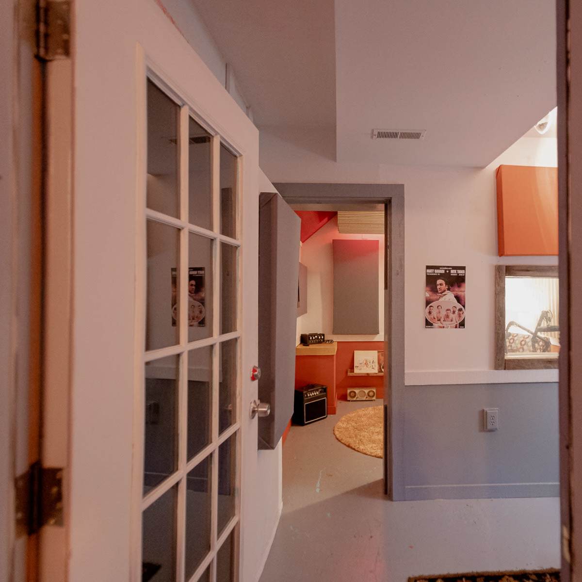A doorway leading into a hallway with light-colored walls, a circular rug, and posters on the walls.
