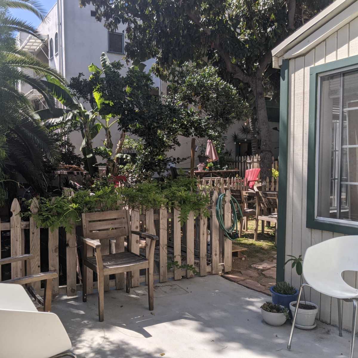 A small outdoor patio area with wooden furniture, a picket fence, and lush greenery surrounding the space.