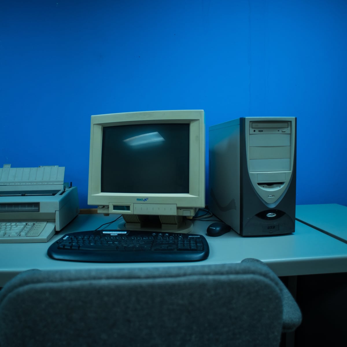 An old computer setup featuring a beige monitor, a printer, and a desktop tower against a blue wall.
