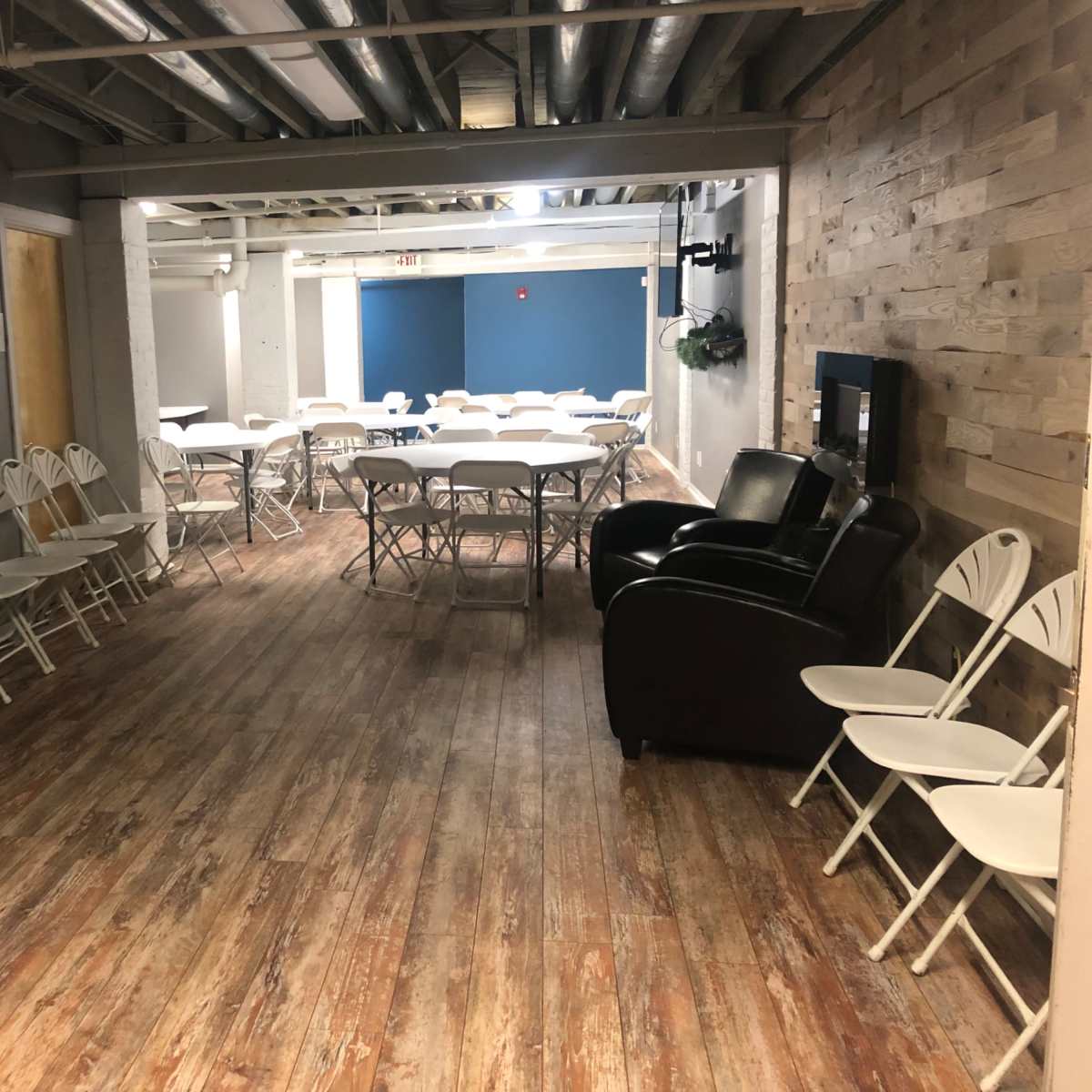 A spacious, well-lit room with folding chairs arranged in rows and several tables set up for an event or gathering.