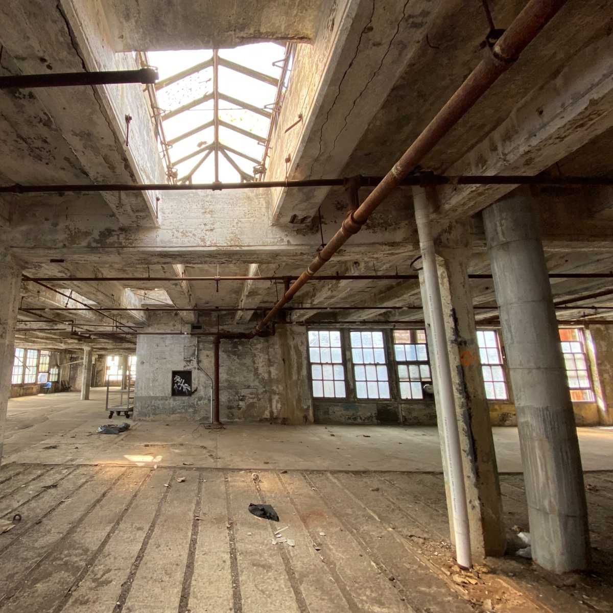An abandoned industrial space with peeling walls, exposed beams, and large windows allowing natural light to enter.