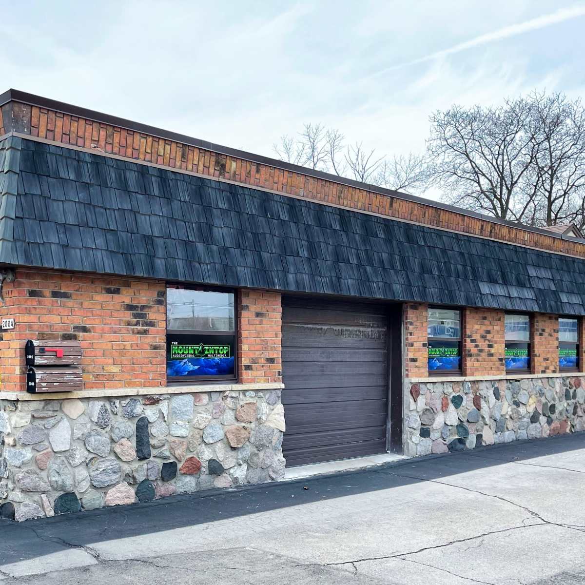 A brick building with a stone foundation, featuring large windows and a dark, shingled roof.