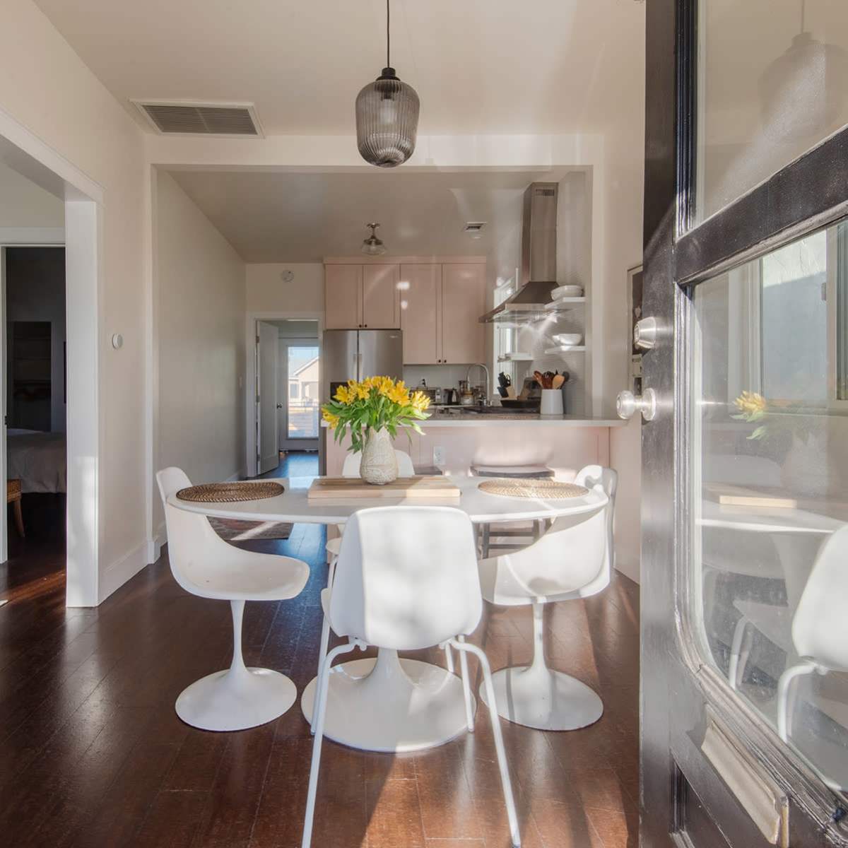 A dining area with a round table and white chairs is visible through a doorway, showcasing a softly lit kitchen in the background.
