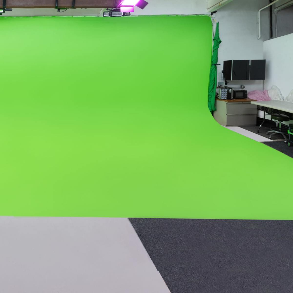 The scene shows a photography studio with a green screen backdrop, white walls, and a white seating area on one side.