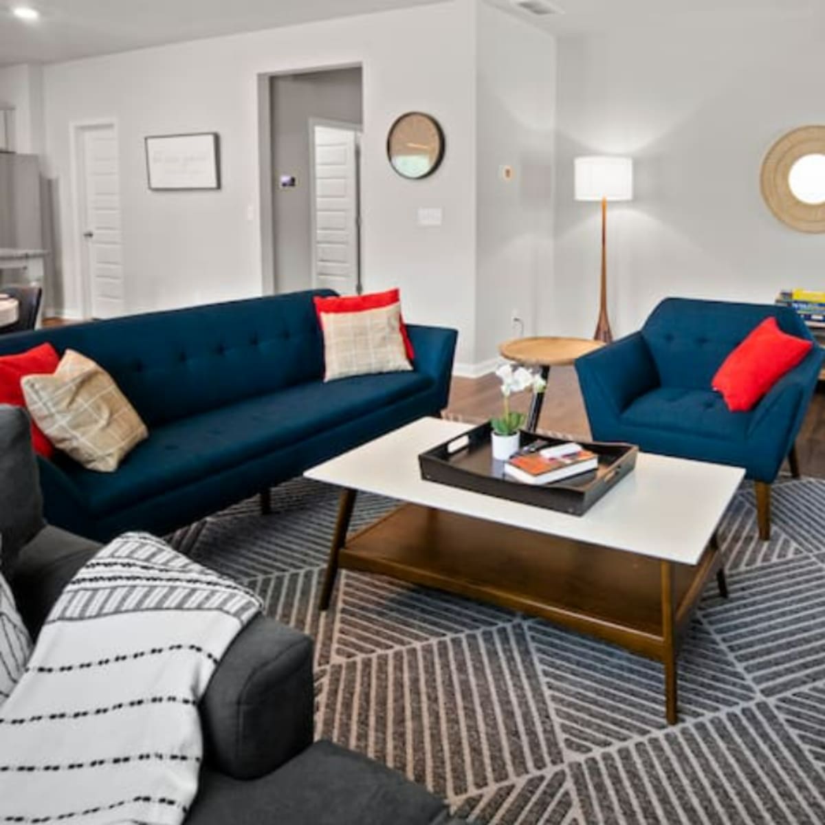 The living room features two teal sofas, a patterned rug, a coffee table with books and a plant, and a staircase visible in the background.
