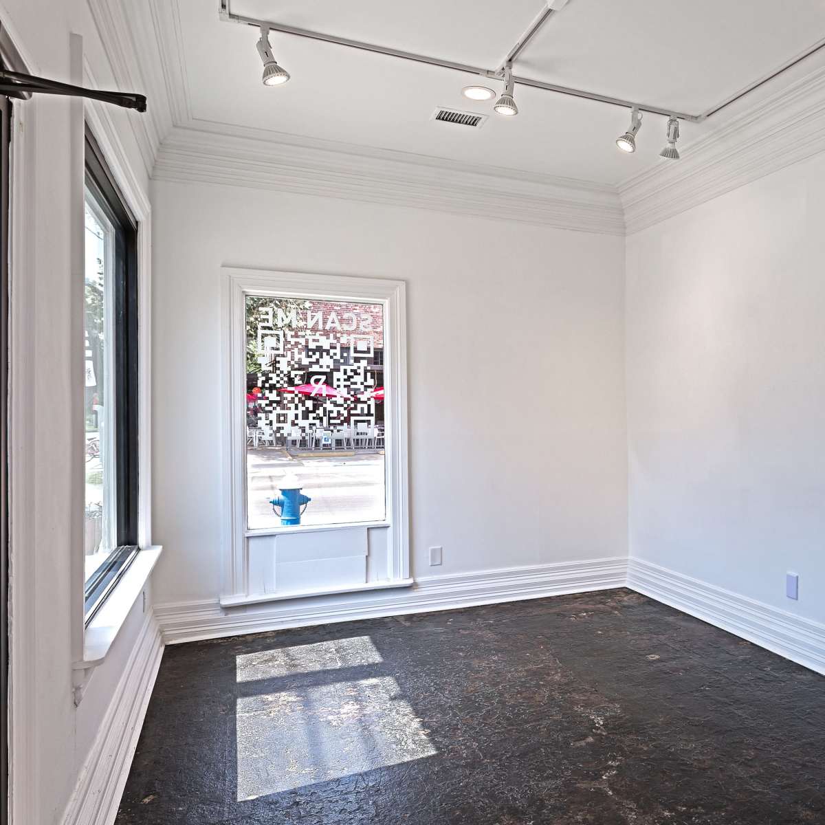 An empty room with white walls, a large window allowing natural light, and a dark floor.