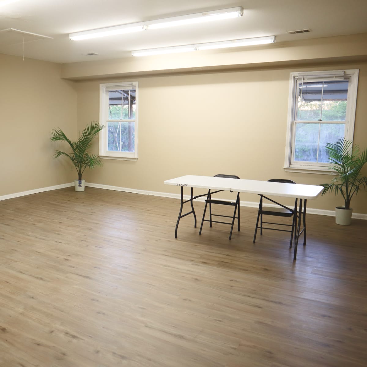 A sparsely furnished room with two windows, a table in the center, and two black chairs facing the table.