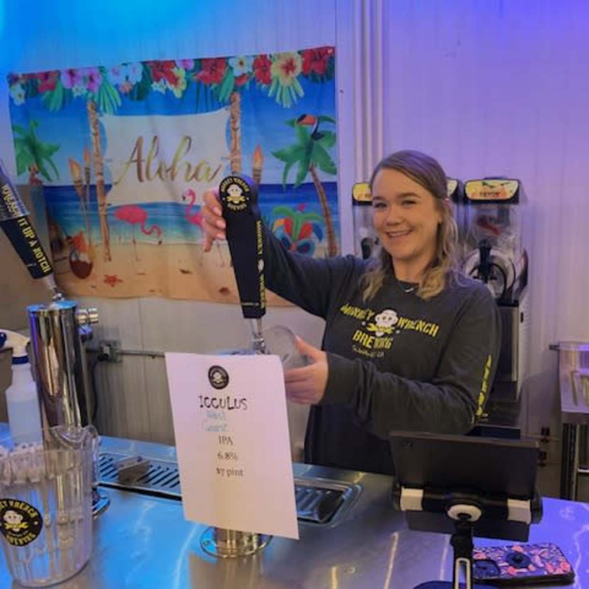 A woman is serving beer from a tap at a bar featuring a tropical-themed backdrop.