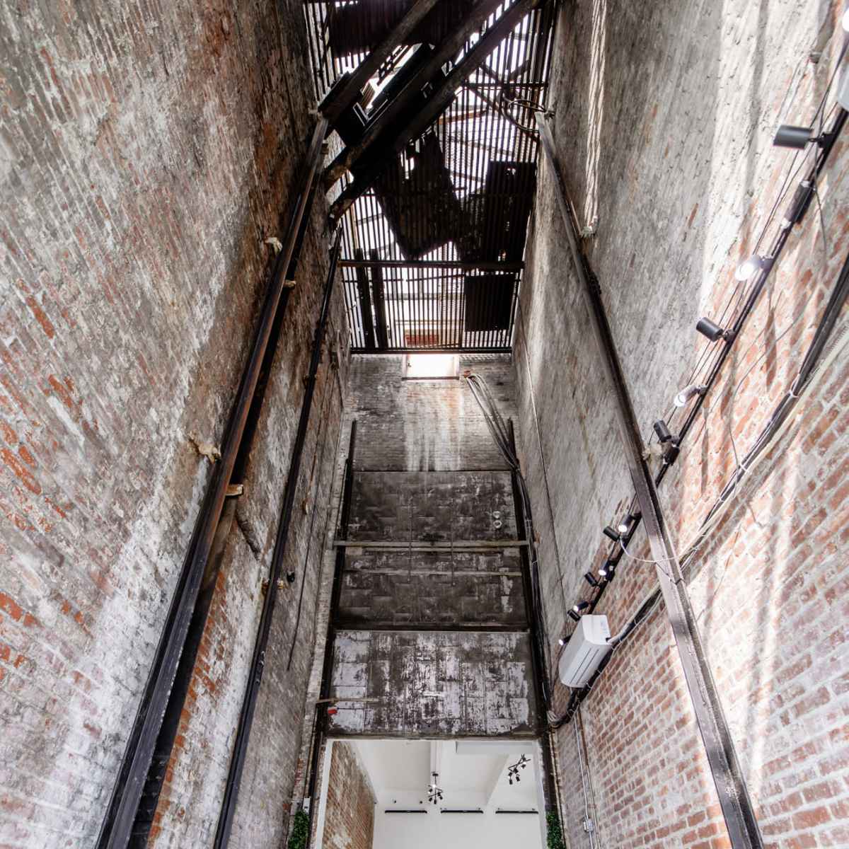A tall, industrial-style interior featuring exposed brick walls, metal beams, and a spacious white floor with a minimalistic backdrop.