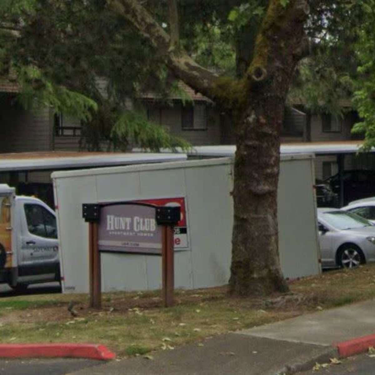 A parking area behind a sign for "Hunt Club" near several cars and trees.