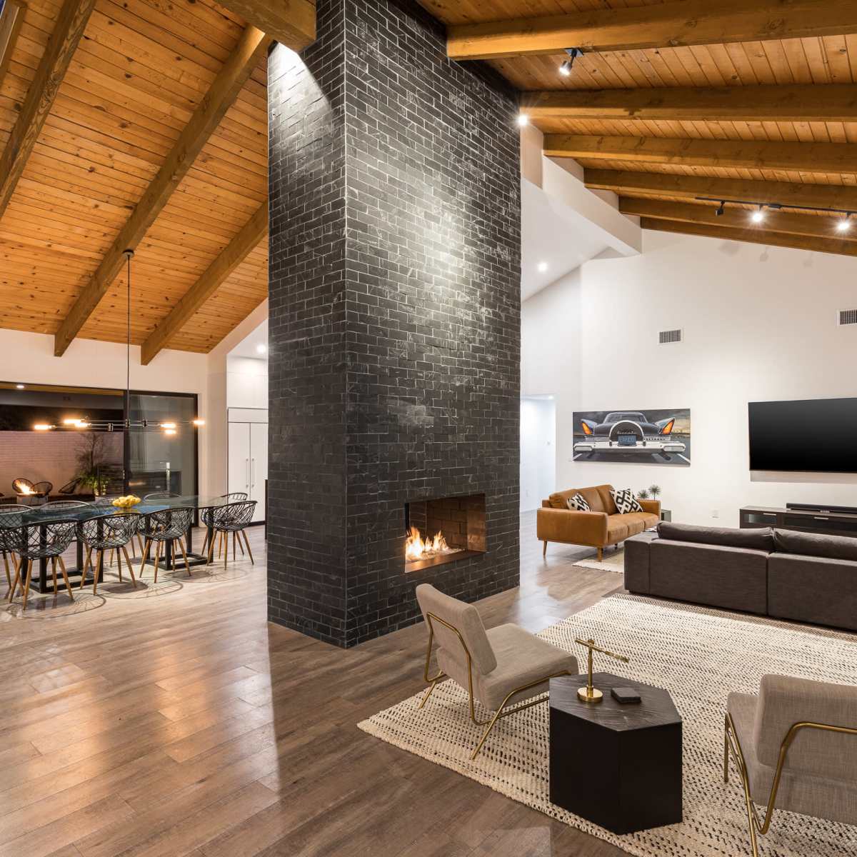 A spacious living area features a black stone fireplace, wooden beams, and a dining space with a round table beside large windows.