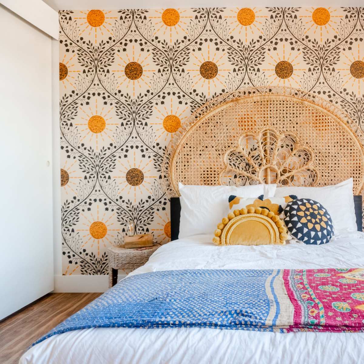 A bedroom with a large patterned wall, a bed adorned with colorful pillows, and a decorative wicker headboard.