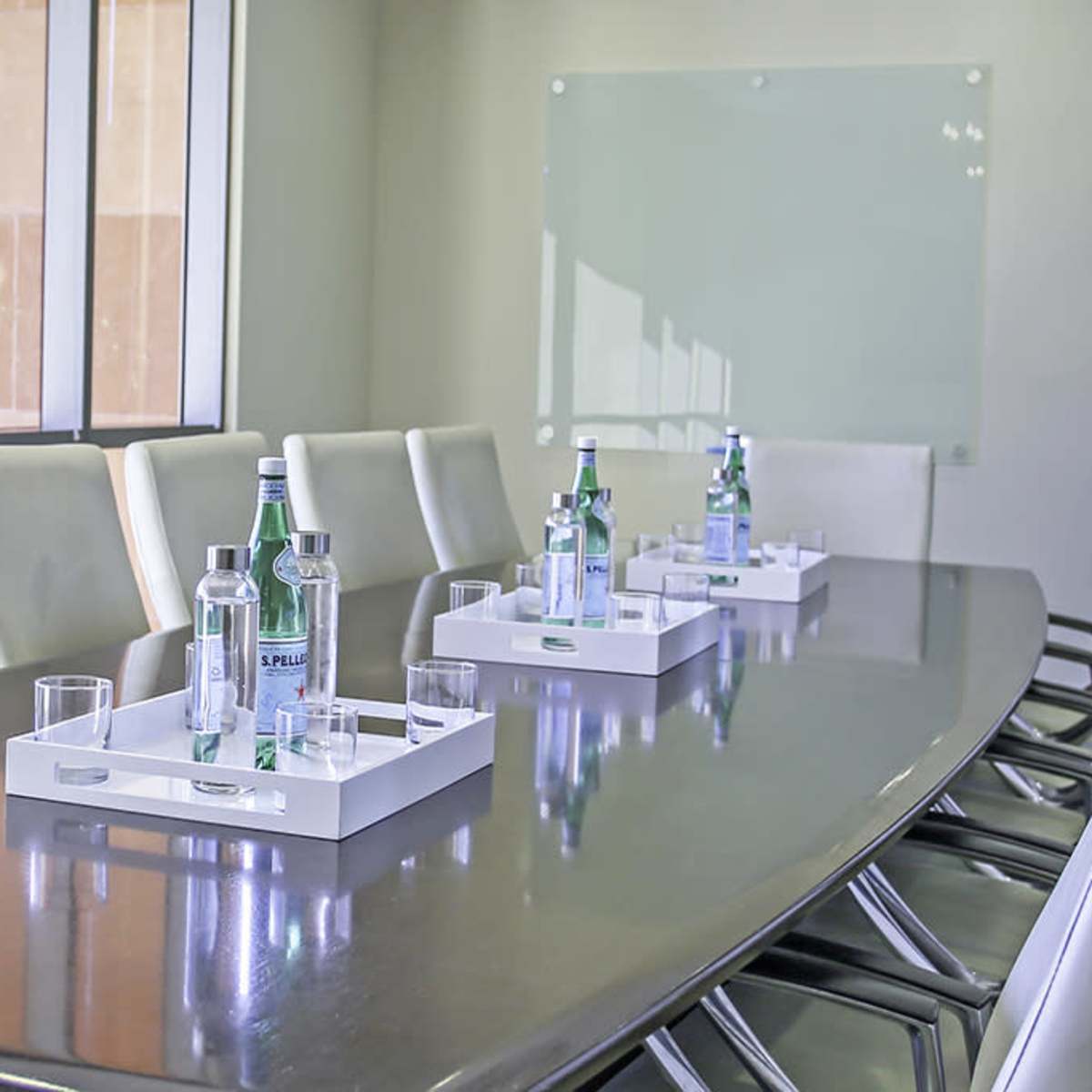 A long conference table is set with water bottles and glasses for a meeting in a brightly lit room.