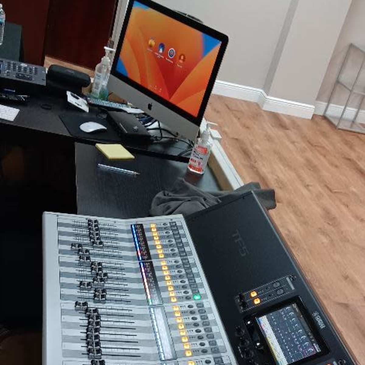 A Yamaha digital audio mixer on a table next to an iMac computer in an office setting with wooden flooring.