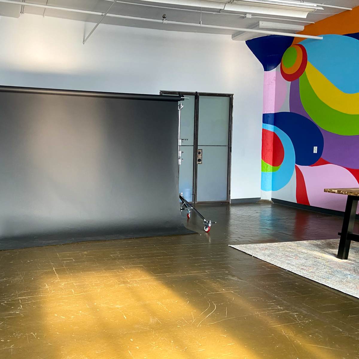 A photography studio with a black backdrop set up against a colorful wall and wooden floor.