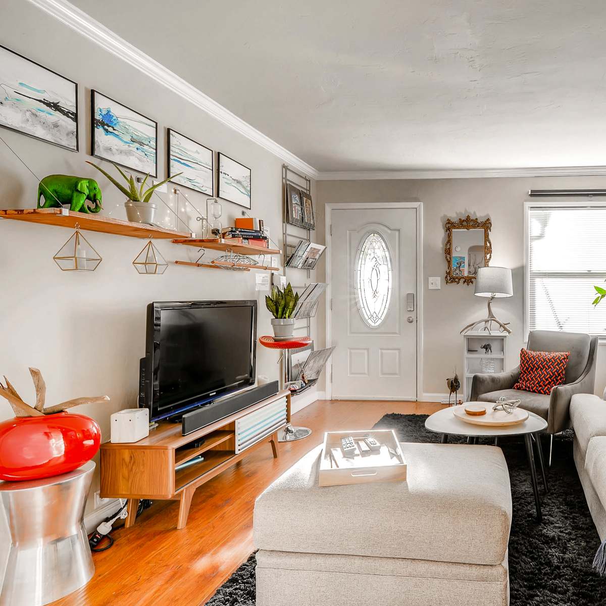 A cozy living room with a grey sofa, a television on a wooden stand, a round coffee table, and decorative plants along with wall art.
