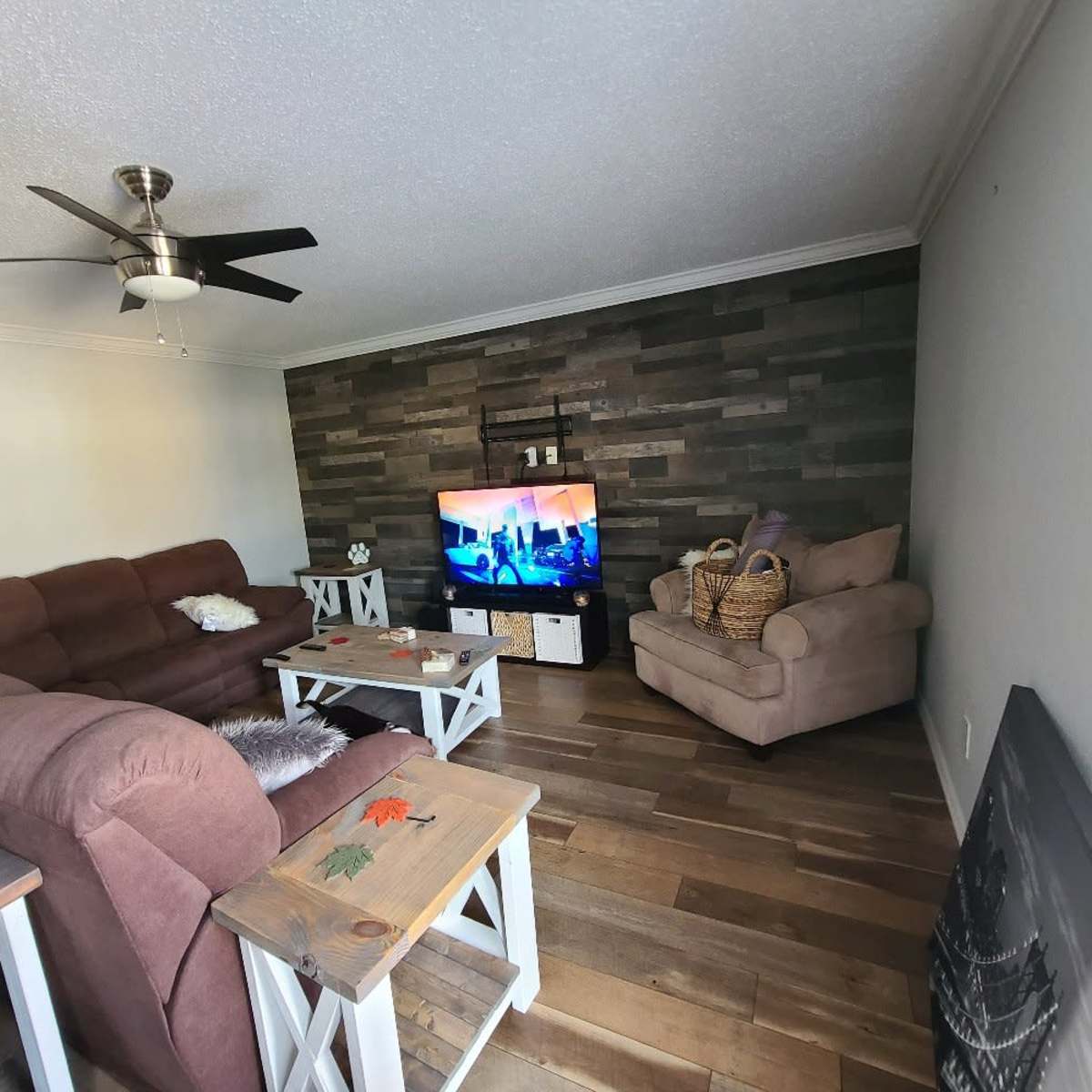 The living room features a brown sectional sofa, a beige armchair, a wooden coffee table, and a television mounted on a stone accent wall.