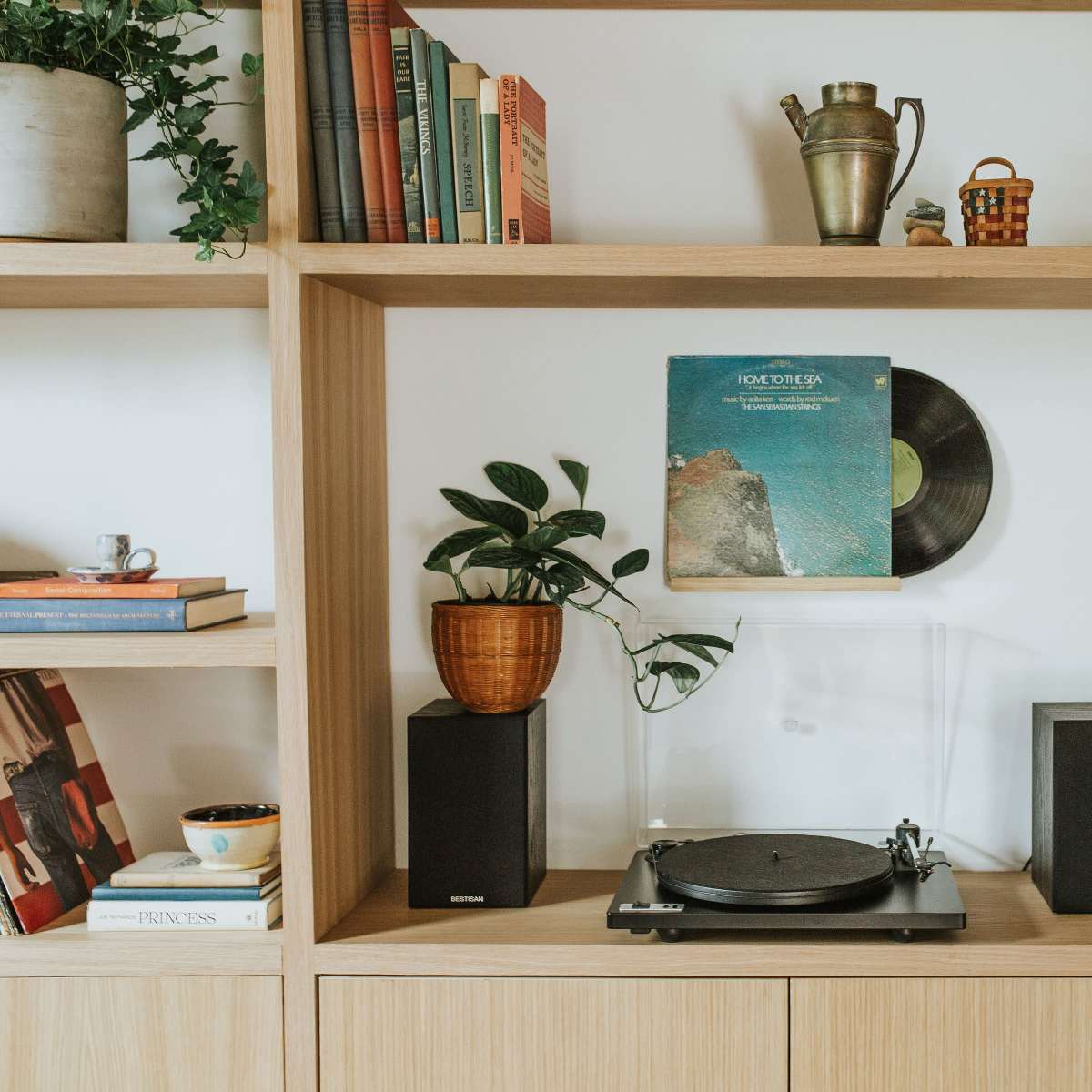 A wooden bookshelf displays books, a globe, a houseplant, and a turntable with a vinyl record on its stand.