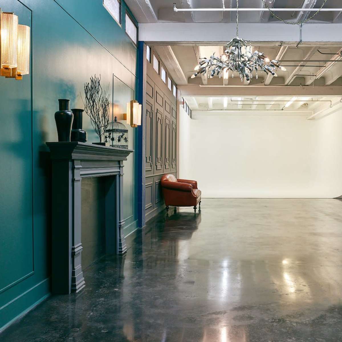 A spacious studio with a polished concrete floor, teal walls, a vintage-style couch, and a well-lit backdrop area.