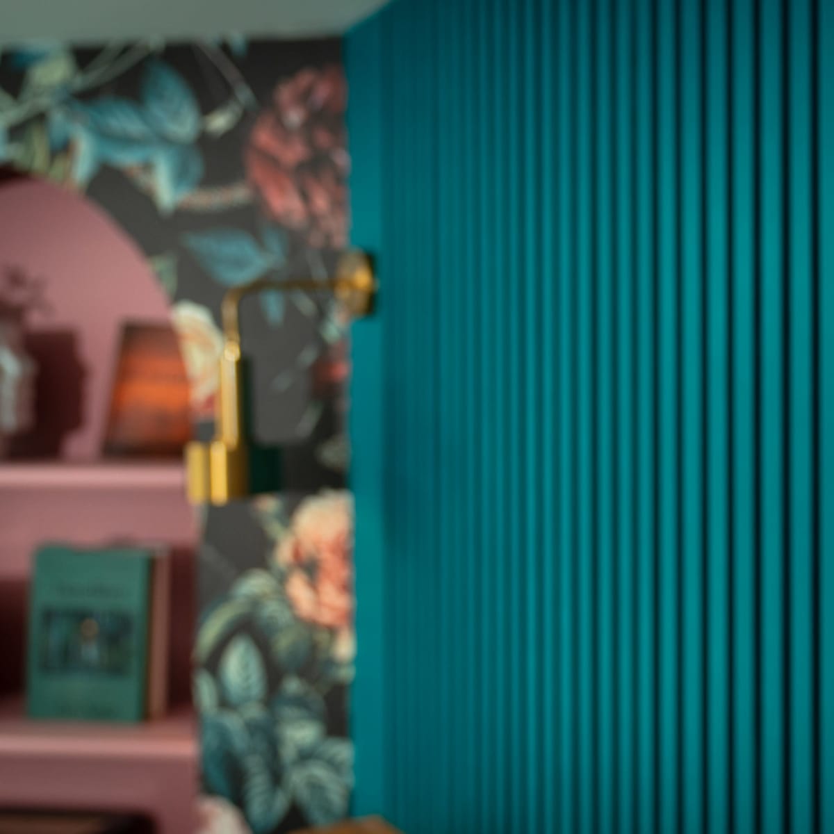 A brass wall sconce is mounted on a teal vertically striped wall, with floral wallpaper visible in the background.