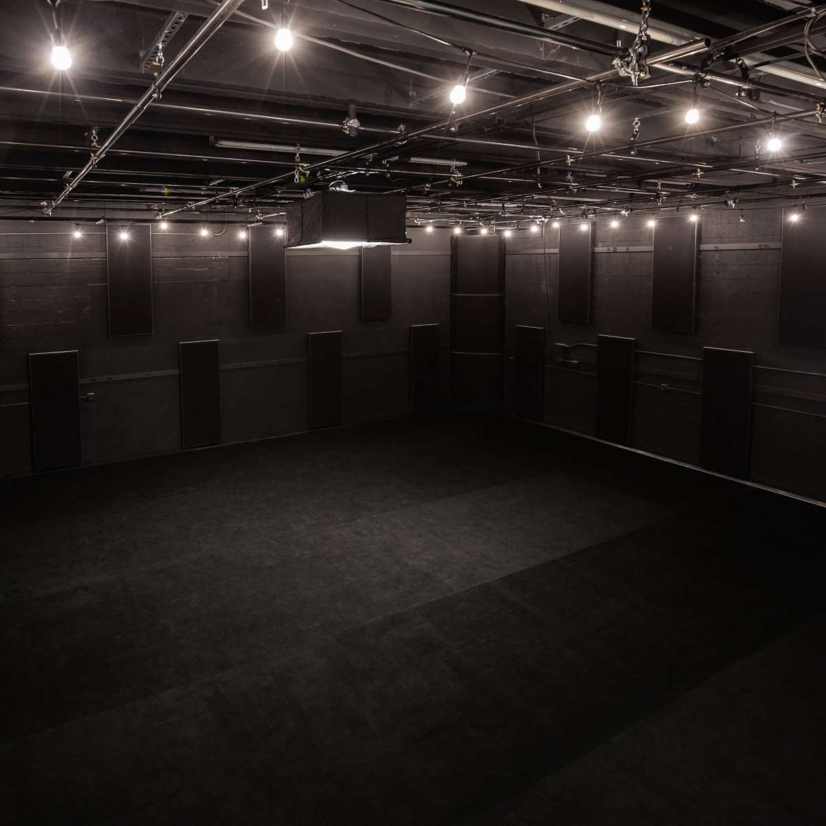 A large, empty black box theater with a flat floor and overhead lights.