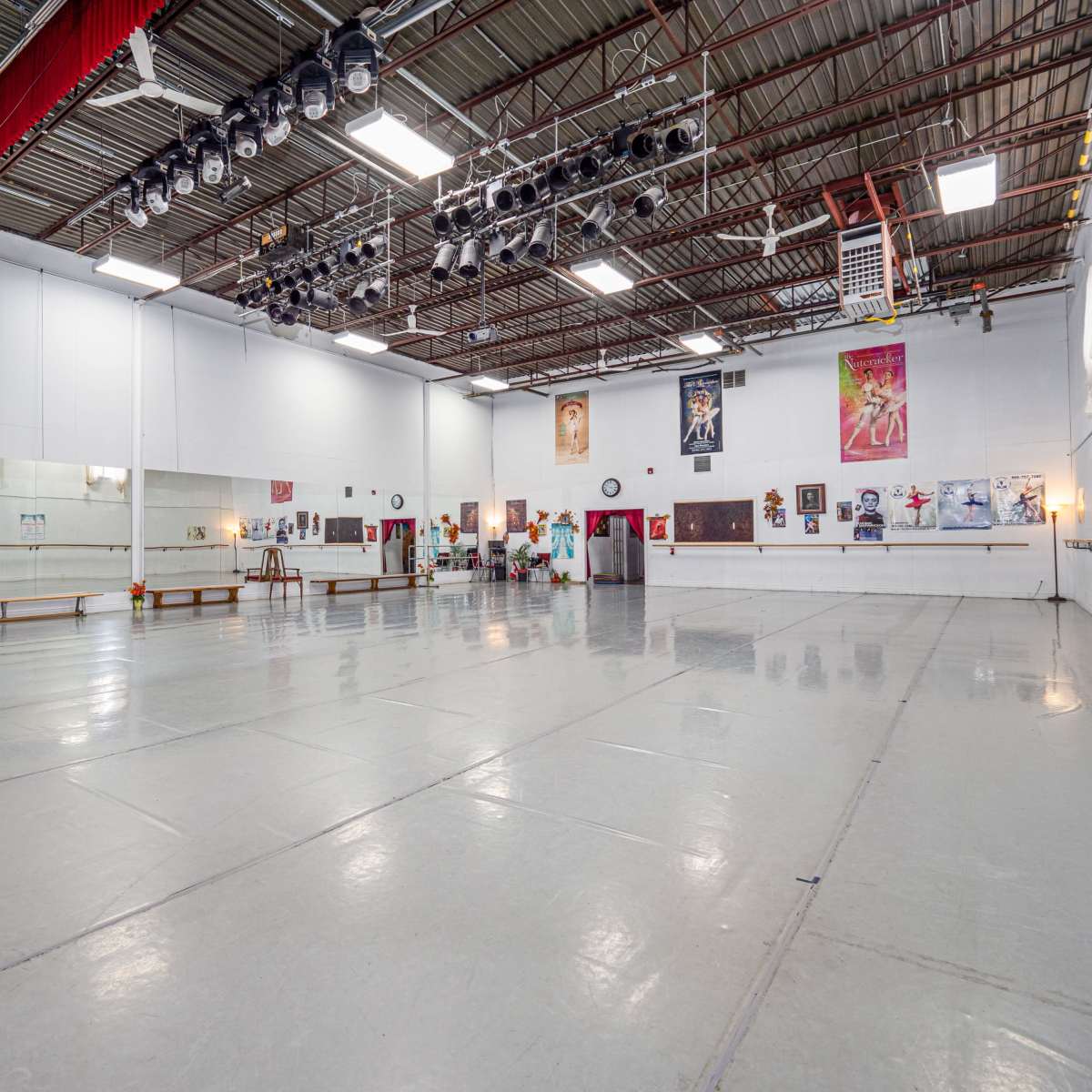 A spacious dance studio with a mirrored wall, wooden ballet bars, and various posters on the walls.