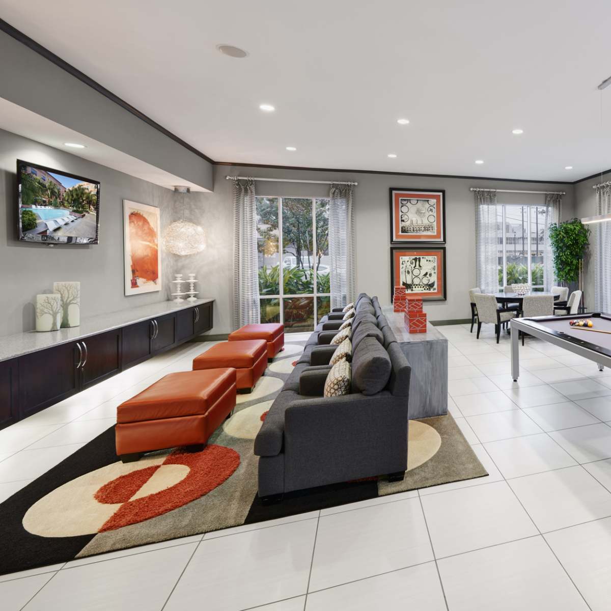 A modern lounge area with a pool table, seating, and large windows overlooking an outdoor view.