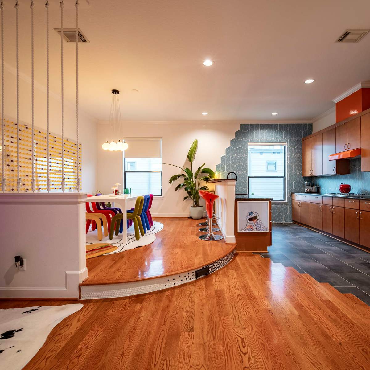 A modern kitchen and dining area featuring colorful chairs, wooden cabinets, and a unique tile backsplash.