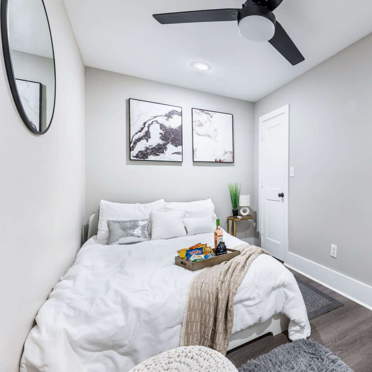 A small, tidy bedroom with a bed, wall art, and a kitchenette visible through an adjoining doorway.