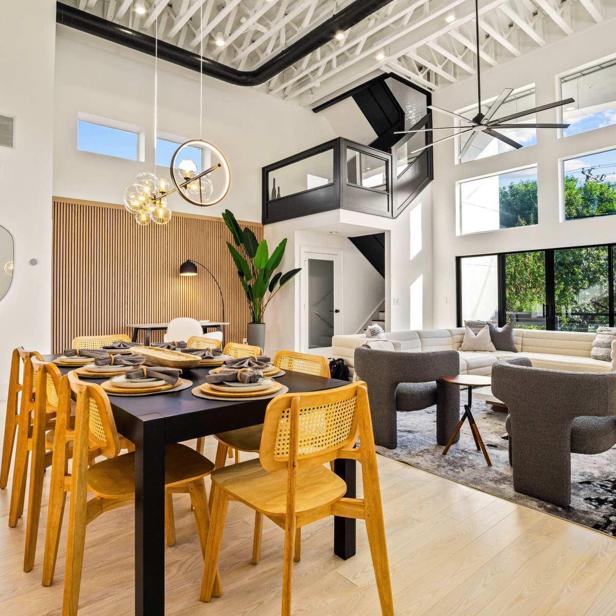 A modern open-concept living and dining area with high ceilings, large windows, and contemporary furnishings.