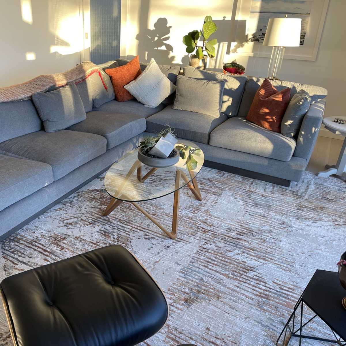 A modern living room with a large gray sectional sofa, a round glass coffee table, and a patterned rug.