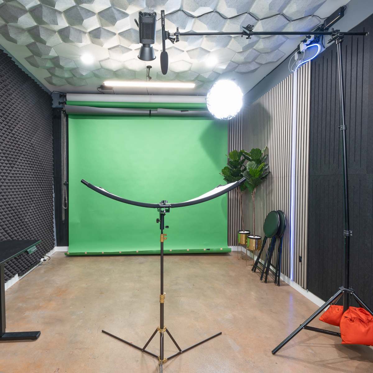 A photography studio equipped with a green backdrop, lighting equipment, and soundproofing panels on the walls.