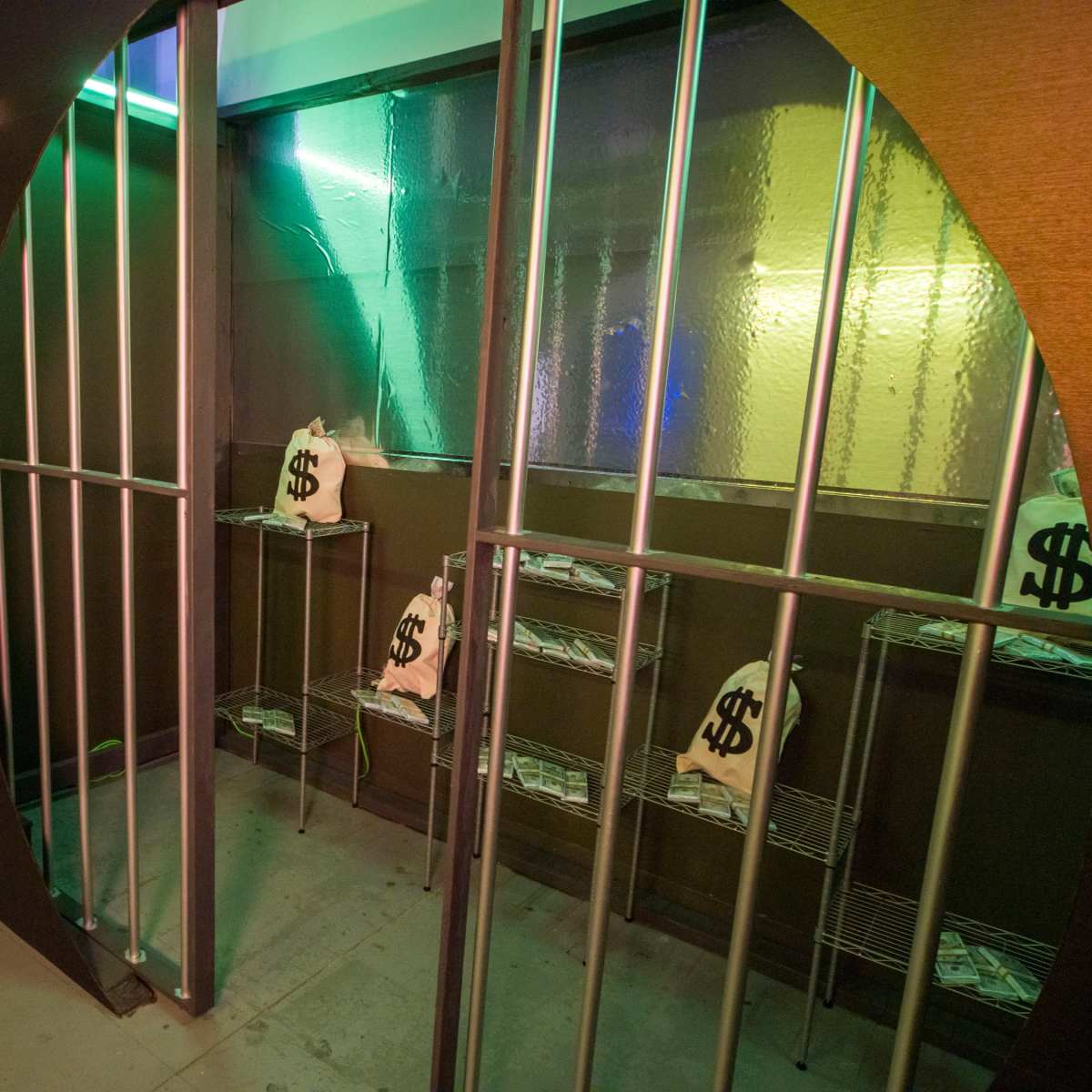 An enclosed room with metallic bars and bags marked with dollar signs inside wire shelving.