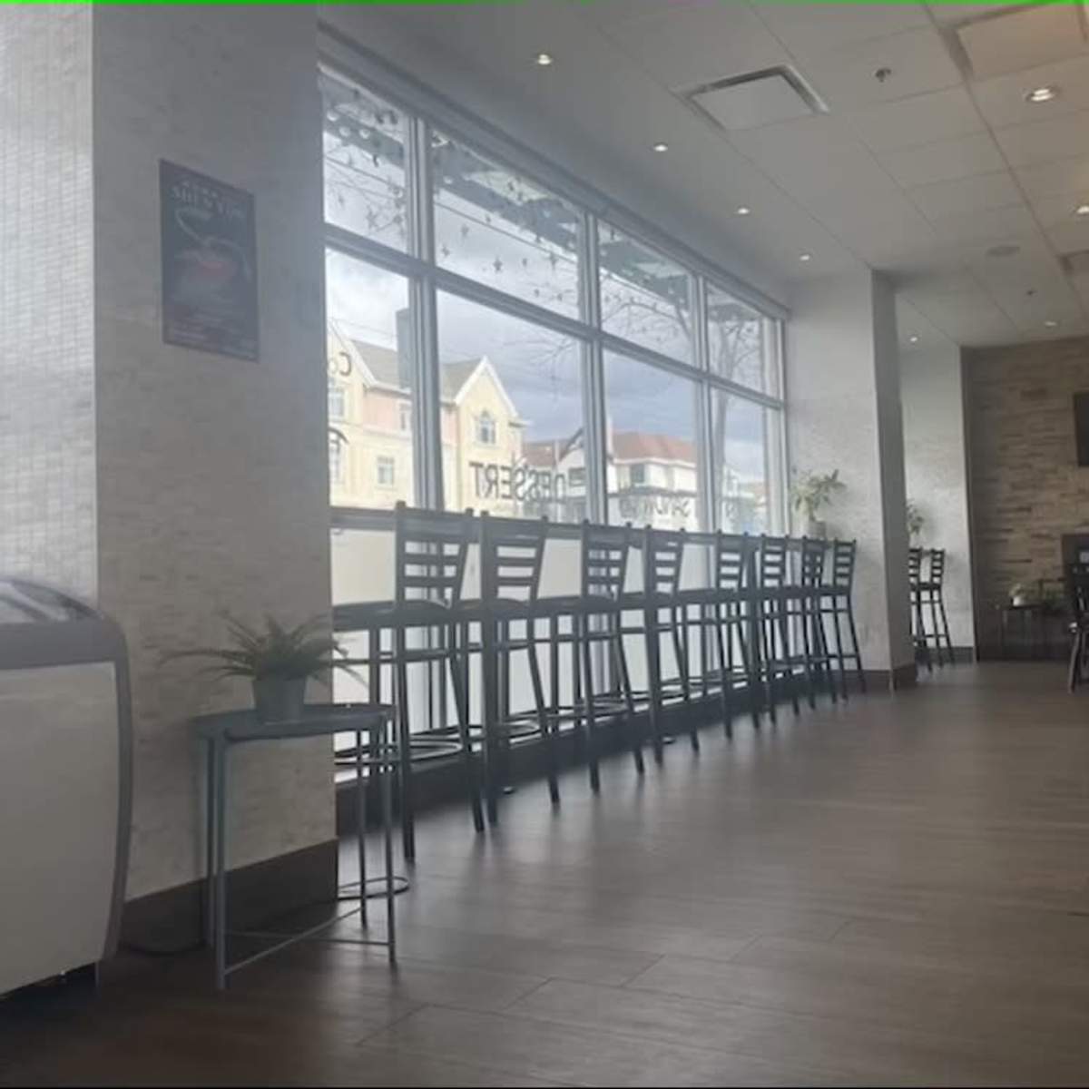 The interior of a café with a row of tall chairs and tables along a large window.