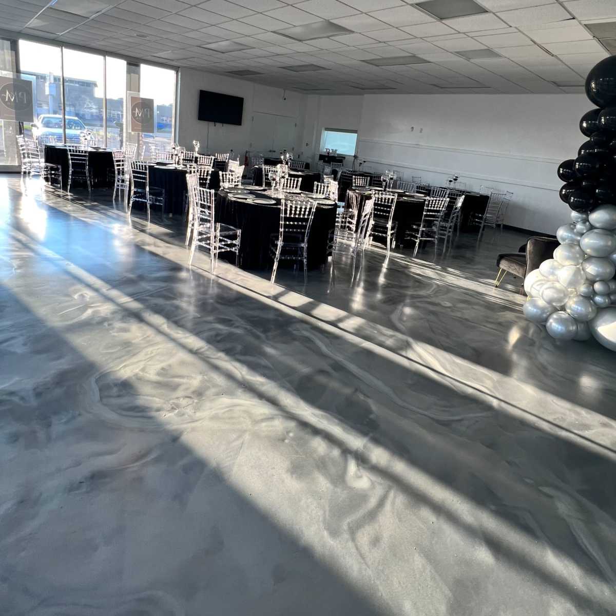 A spacious indoor event venue with several tables set up, surrounded by black and white balloon decorations.