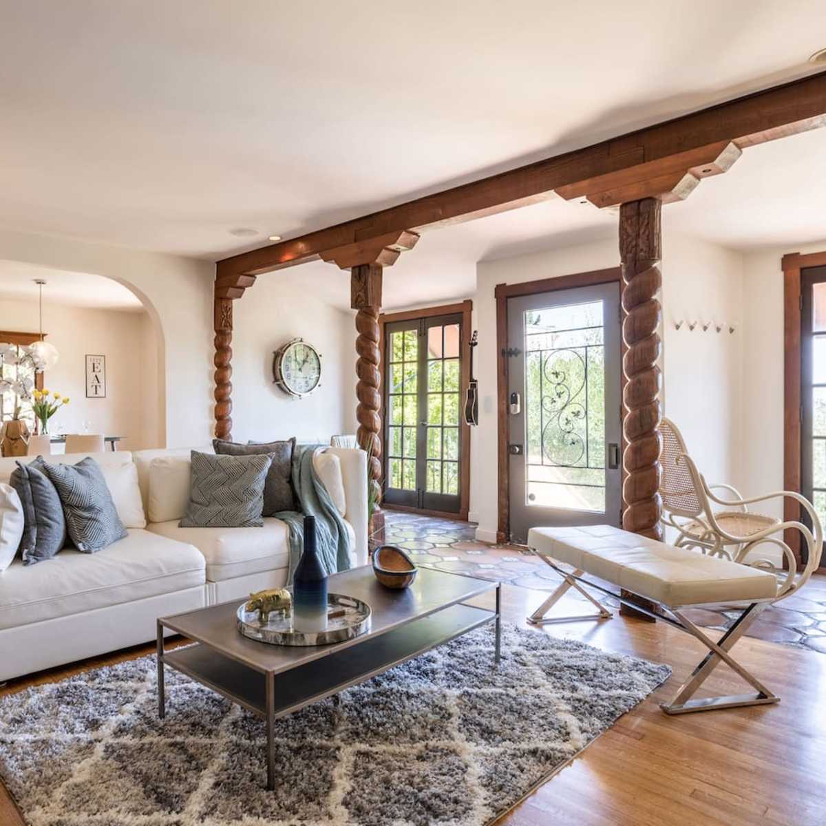 A living room with a white sofa, a glass coffee table, and large windows featuring wooden beams and a tiled floor.