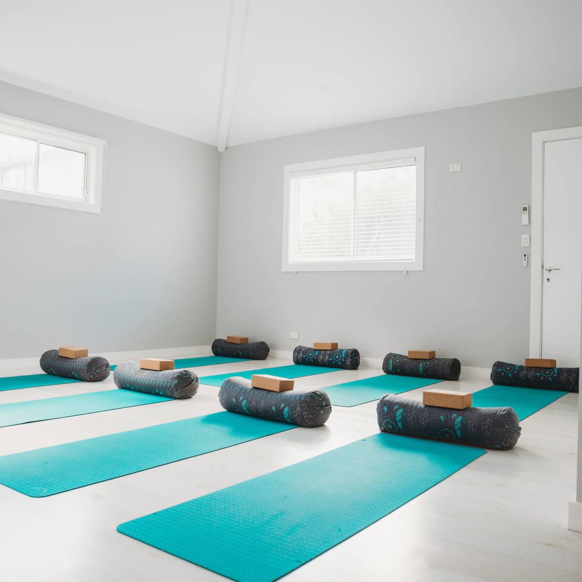 A yoga studio with several blue mats arranged on the floor, each topped with a bolster and block.