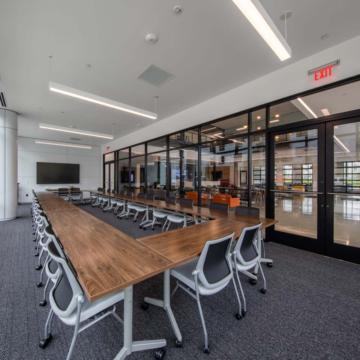 A modern conference room features a long wooden table surrounded by ergonomic chairs, with large windows allowing natural light to fill the space.