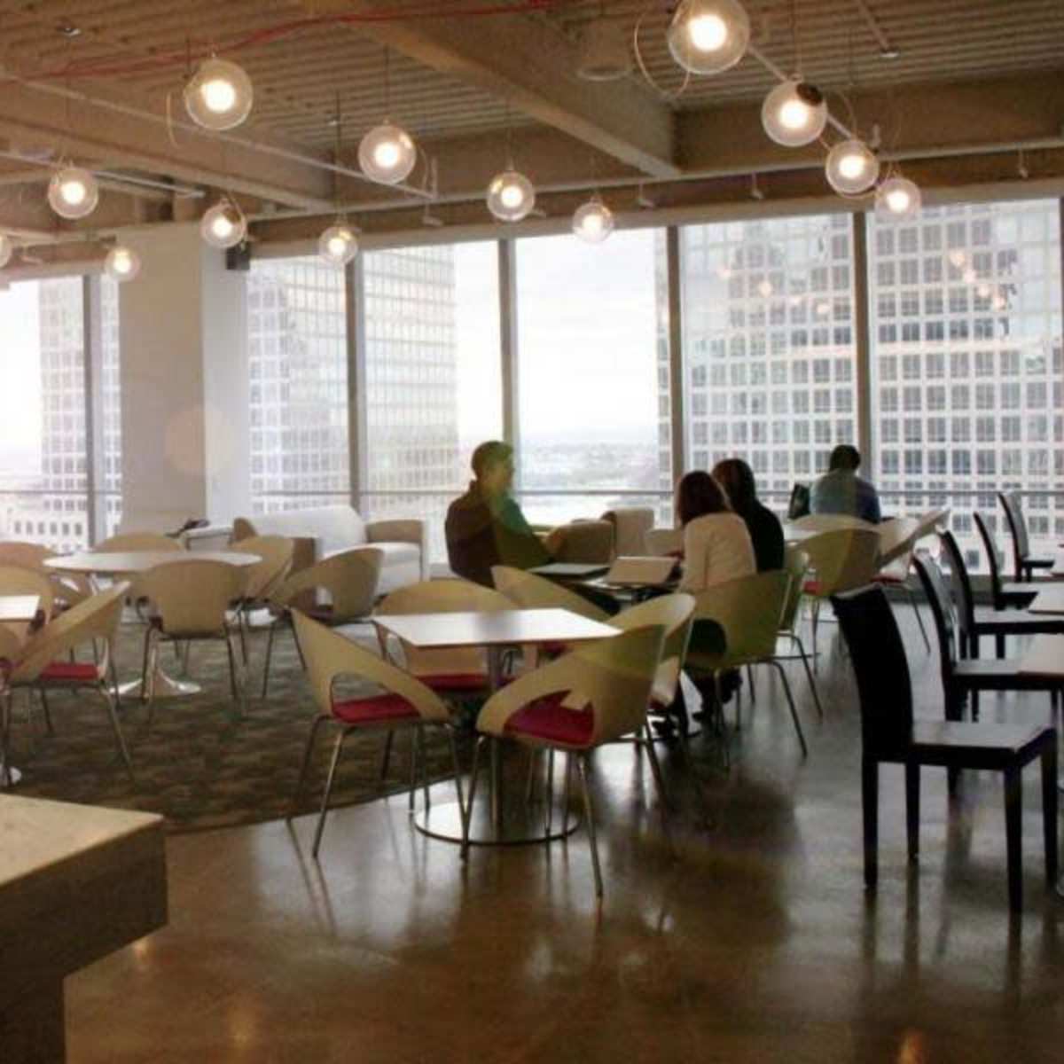 A spacious office break area with modern furniture, large windows, and pendant lighting.