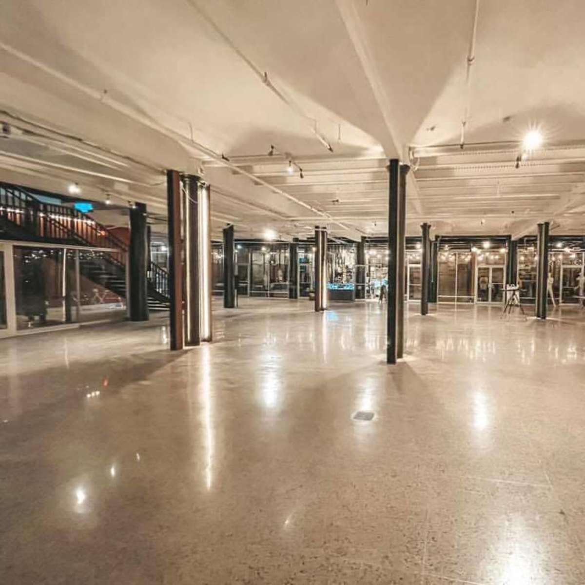 A spacious, empty interior with polished concrete flooring and several columns, illuminated by overhead lights.