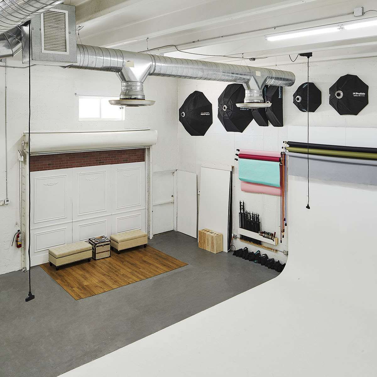 A spacious photography studio featuring a white backdrop, various lighting equipment, and a seating area with a wooden floor.